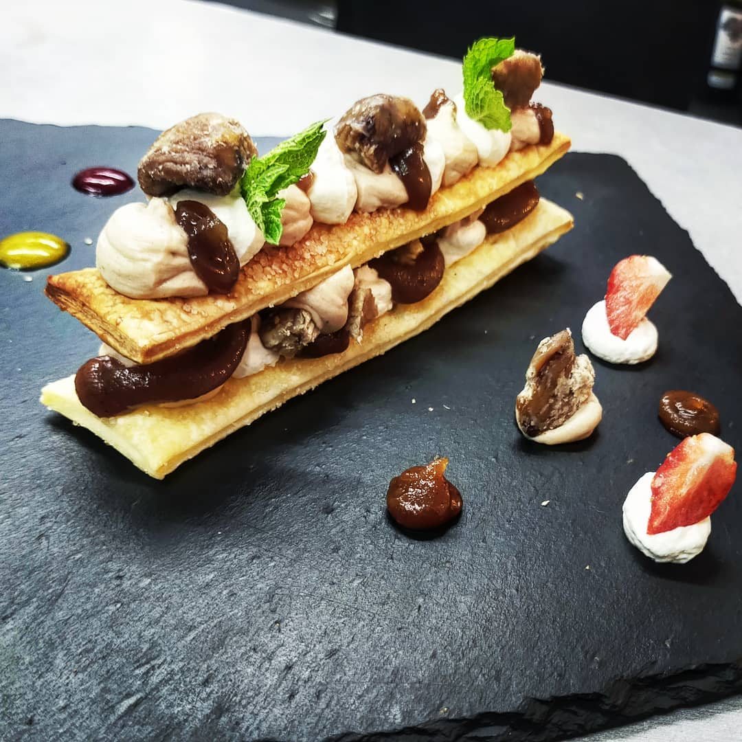 Un mille-feuille aux marrons, crème et feuille de menthe, dressé sur une ardoise avec des fraises et de petites touches de crème